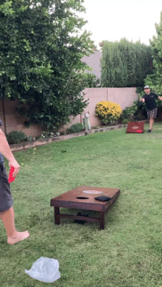 two men are playing cornhole in the backyard