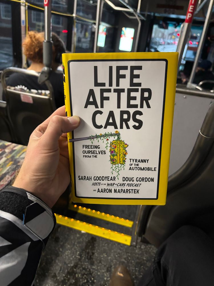 POV of a person holding the hardcover book “Life After Cars” featuring an illustration of a traffic light overgrown with vines. In the background is the interior of a transit bus.

LIFE AFTER CARS
FREEING OURSELVES FROM THE
TYRANNY OF THE
AUTOMOBILE
SARAH GOODYEAR DOUG GORDON
HOSTS -THE WAR ON CARS PODCAST
* AARON NAPARSTEK