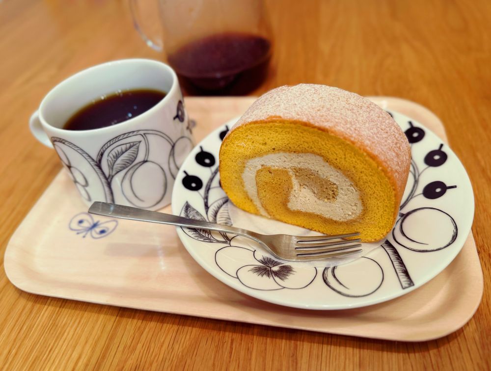 ほうじ茶ロールケーキとコーヒーの写真。ロールケーキのクリームはほうじ茶具合によって二層になっており、中心部は茶色が濃くなっている。