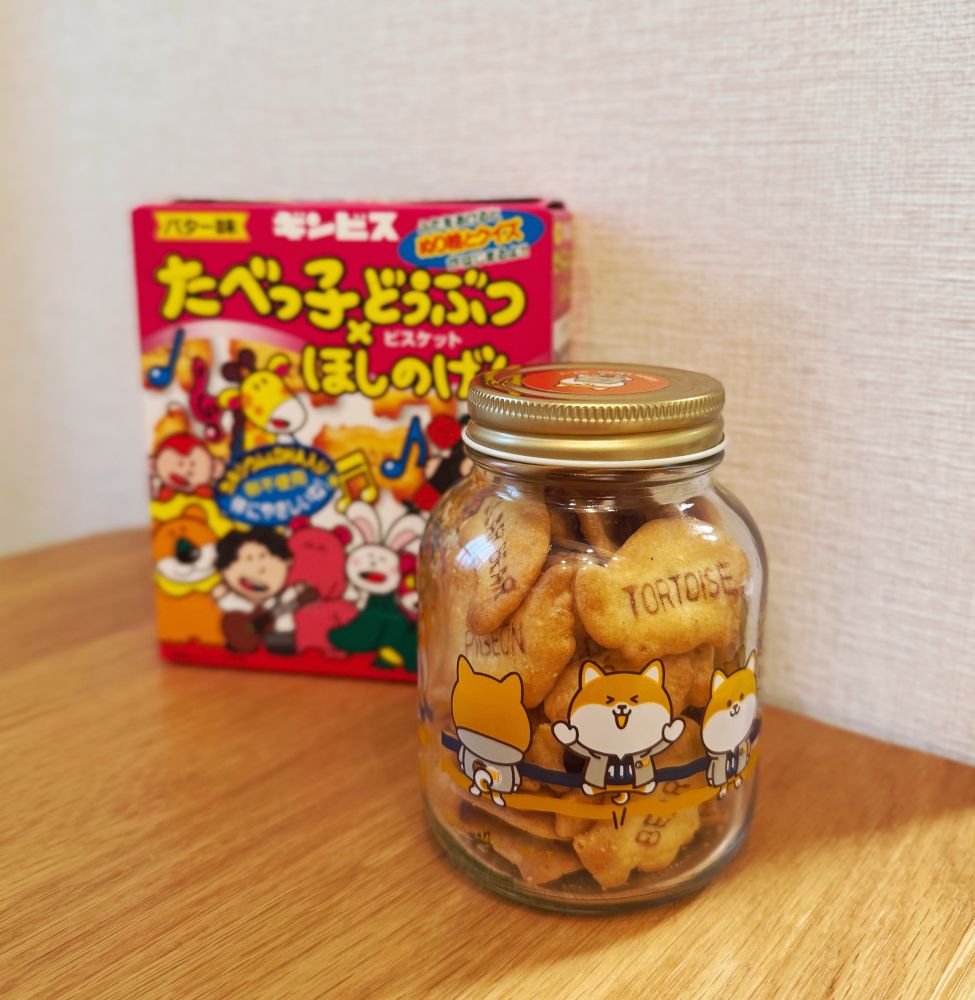 いろいろなポーズのポリまるがデザインされている瓶に入ったたべっ子どうぶつビスケットの写真。ビンの後方には、星野源さんとのコラボパッケージのたべっ子どうぶつの箱が置かれている。