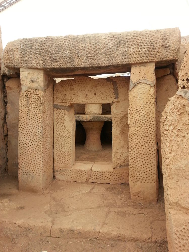 Three large pecked stones, two uprights and a lintel, surround four similar but smaller stones, through which a rectangular opening or niche can be seen.