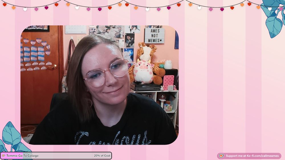 Ames' facecam over their just chatting scene. The background behind their facecam is pink striped and there are lesbian flag colored heart lights at the top. There is a kofi goal with 'Temmie go to college' on it in the lower left corner and Support me at ko-fi.com/callmeames on the right. They are smiling and wearing a black shirt that says cowboys in white font. Behind them is a pink wall covered in kpop posters and baldur's gate 3 art. There is pink cow squishmallow and a giraffe stuffed animal sitting on top of a cube organizer with various knicknacks.