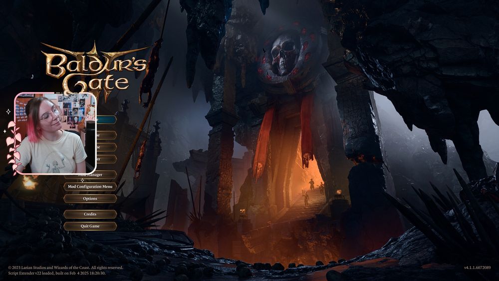 Ames' facecam over the main screen for baldur's gate 3. Around their face cam is a light pink border with pink leaves and a crescent moon. They are smiling with their head tilted and wearing a light pink shirt with a skeleton on it.
