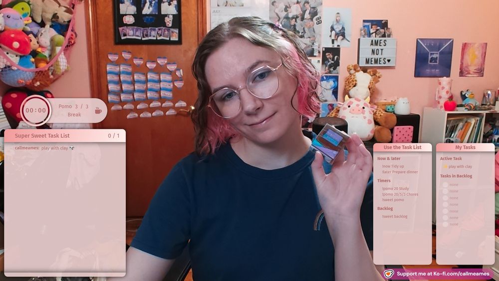 Ames smiling with her head tilted and holding a package of brown sculpy clay. Their hair is wavy and held back with butterfly clips. The super sweet bot overlays are on either side of them in a pink color scheme.