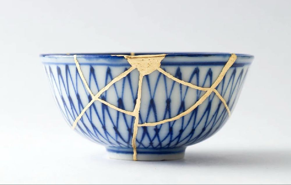 Photo of a white and blue ceramic bowl that has been broken and put back together with visible gold lines where the cracks were.