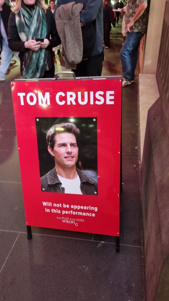 An image of an A frame board that says "Tom Cruise... will not be appearing in this performance" from The Play That Goes Wrong