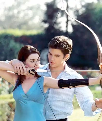 Image is of Anne Hathaway as Mia Thermopolis (Princes Diaries) wearing a blue top and drawing back a bow and arrow with Chris Pine assisting her
