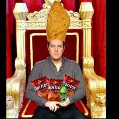 Geoff Keighley with a big dorito for a pope hat, sitting on a massive golden throne and holding several bags of doritos. Praise be his name, the Dorito Pope