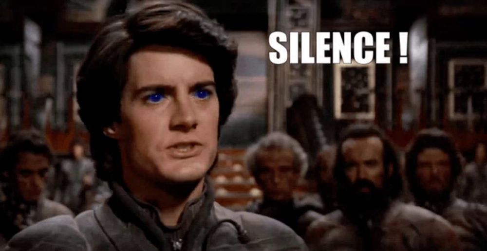 a man with blue eyes is standing in front of a group of men and says silence