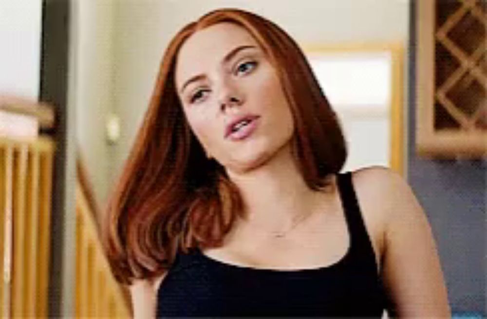 a woman with red hair is standing in a kitchen wearing a black tank top .