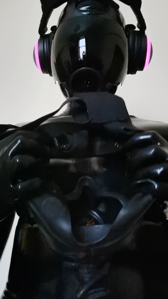 A black latex drone in an MSA Millenium gas mask putting a second mask in position to be placed over the viewer's head. Much rubber fun! 