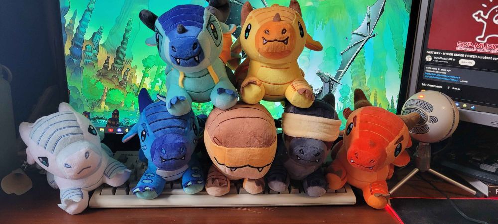 Photo of a collection of plush dragons with various colours and designs. All of them resemble dragons from the series Wings Of Fire.