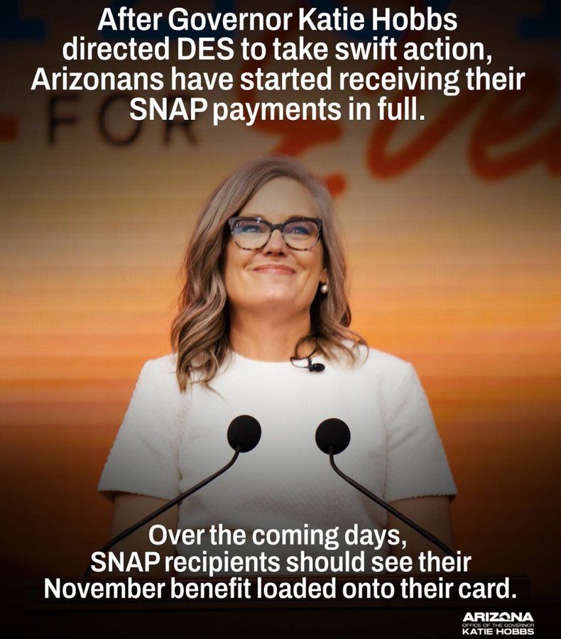 Governor Katie Hobbs stands smiling at a podium with two microphones, wearing glasses and a white outfit, in front of an orange background with blurred text. The image includes a message that reads: “After Governor Katie Hobbs directed DES to take swift action, Arizonans have started receiving their SNAP payments in full. Over the coming days, SNAP recipients should see their November benefit loaded onto their card.” The Arizona Office of the Governor logo is visible at the bottom right