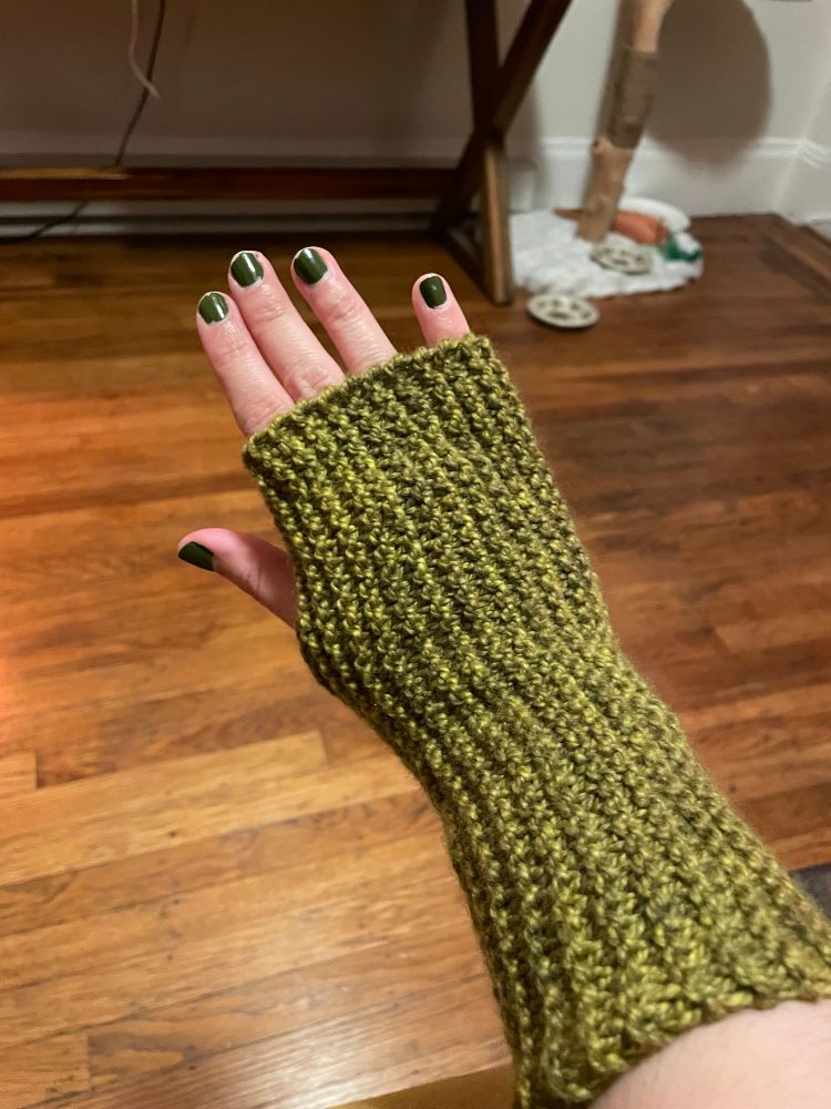 An olive toned arm wearing a mossy green hand knitted arm warmer
