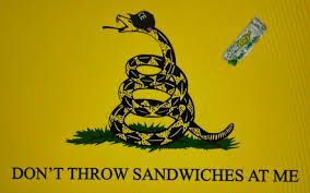 Yellow don’t tread on me snake flag. Snake wearing ICE hat. Subway sandwich being tossed at snake. Text reads don’t throw sandwiches at me