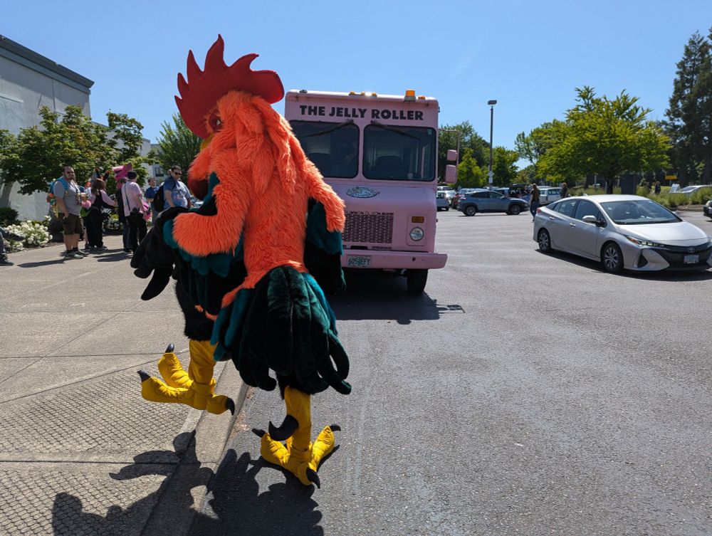 Rochester Rooster struts onto a curb in front of the Voodoo Donuts truck that arrived at the PDX Sheridan