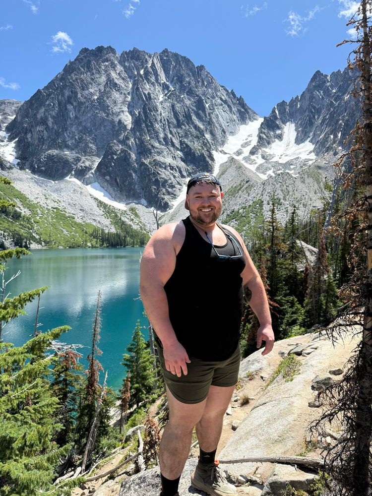 Large man in a tank top hiking near an alpine lake