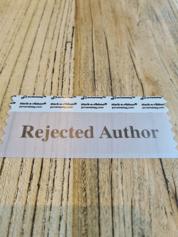 White translucent badge tag on a wooden table that says rejected author 