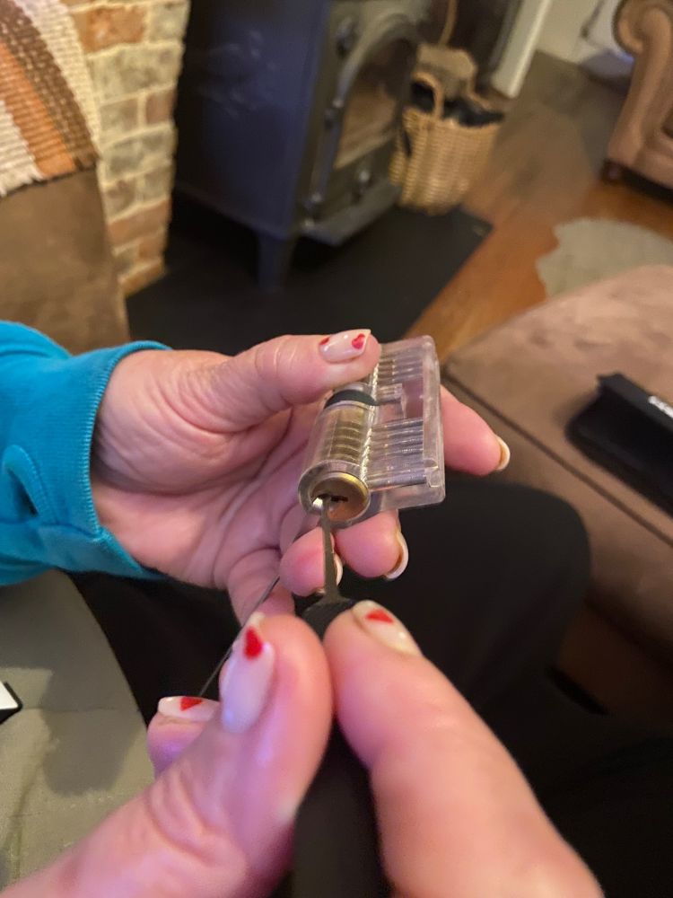 A woman’s hands. She is holding a see-through plastic practice lock in one hand and a pick in the other