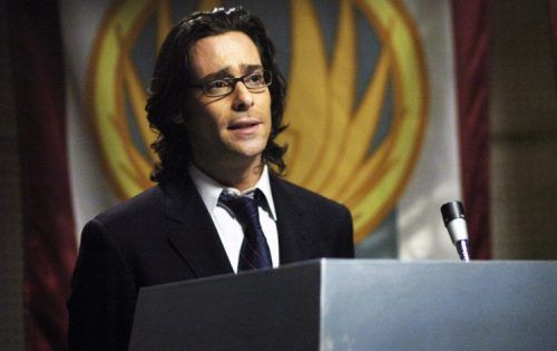 Gaius Baltar (James Callis) speaks into a microphone behind a podium