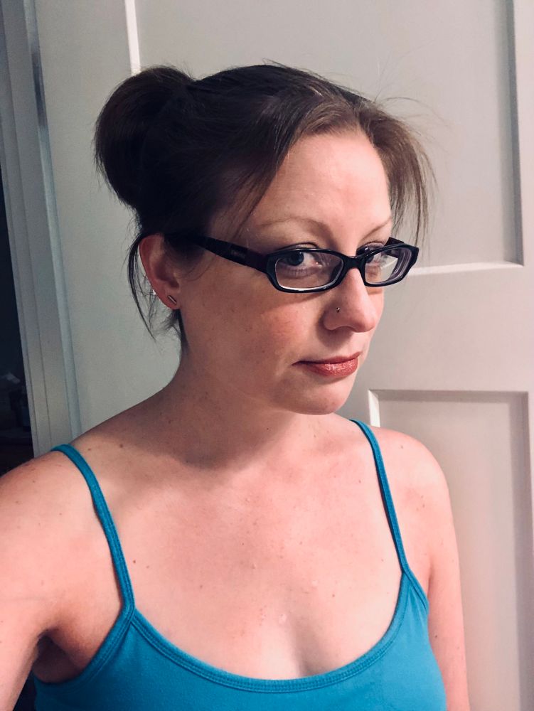 My dumb face (a plain and average-looking brunette gal with glasses) peering sidelong at the camera in front of a white door 