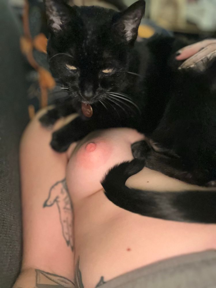 A black cat rests upon Rae’s topless torso