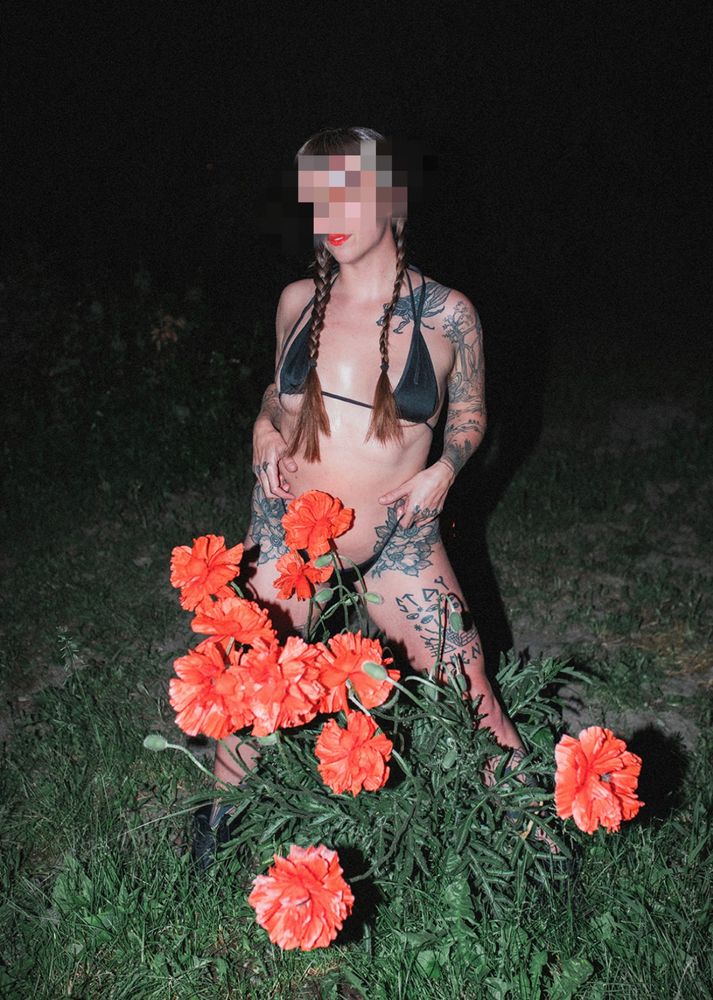 Rae, a kinky GFE FSSW, stands in front of a patch of blooming poppies. She wears a black bikini and has many tattoos. 