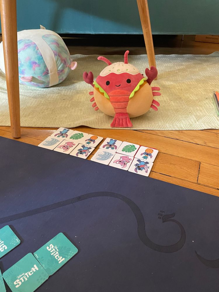 a lobster squishmallow sits on the floor in front of a completed limo and stitch memory card game