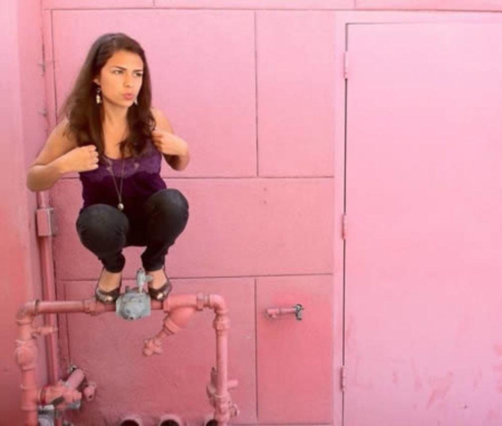 A woman perched on a horizontal drain pipe a few feet off the ground, crouched over, "owling". 