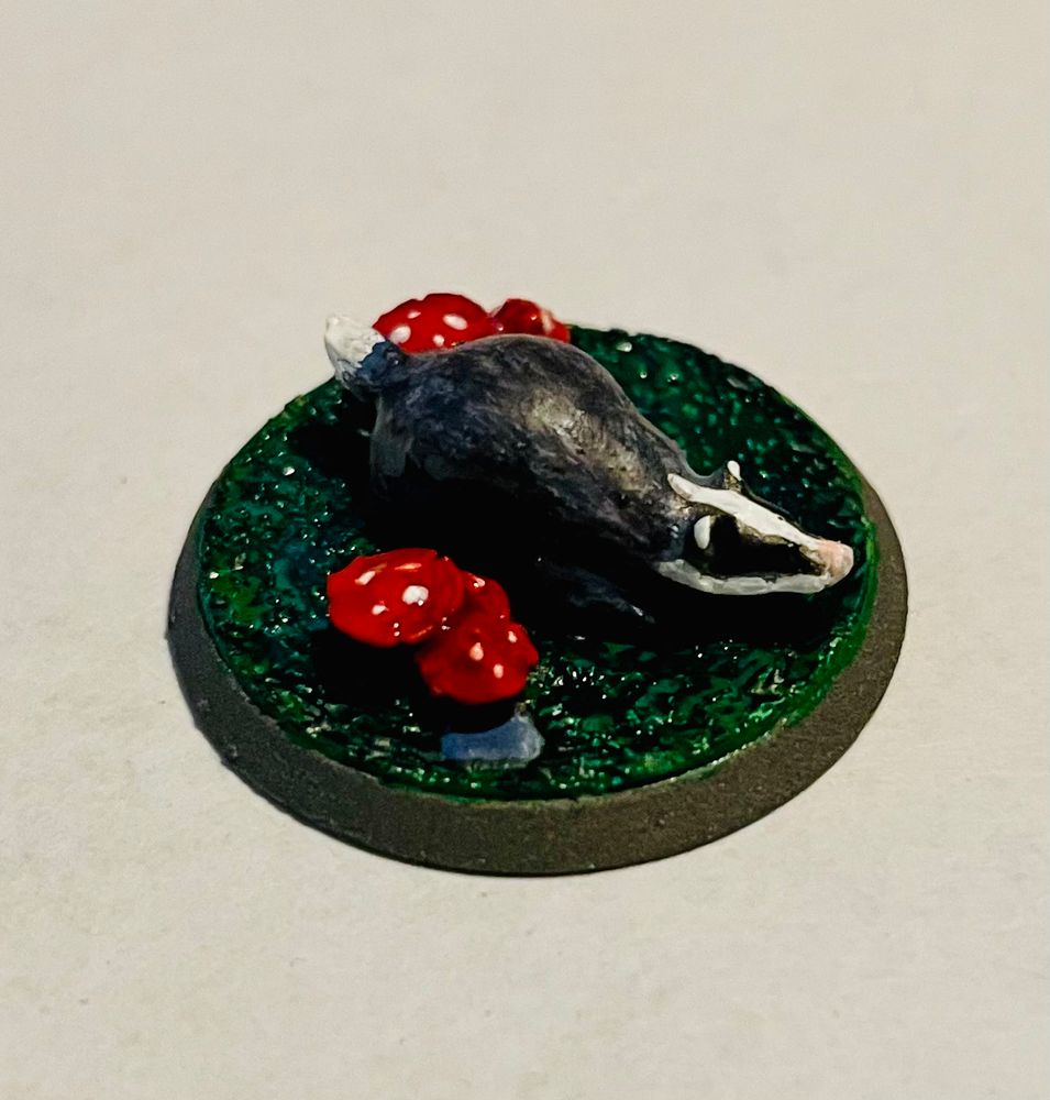Badger figure for table-top role playing games, standing on a round pedestal painted green, flanked by red mushrooms.