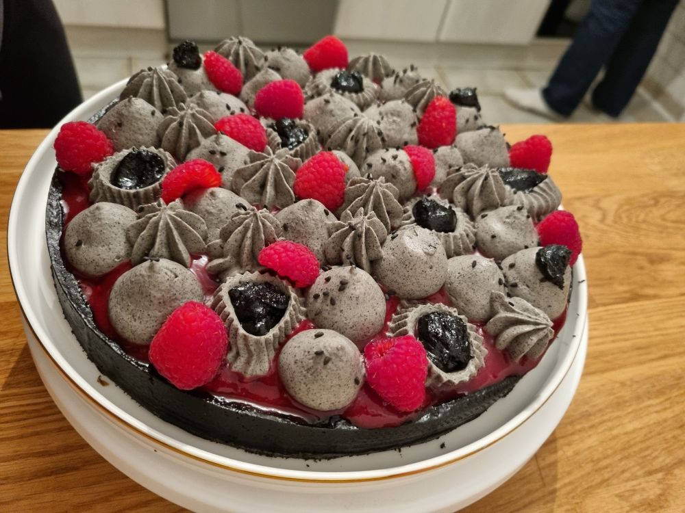 Tarte avec une base noire, de la crème couleur grise due au sesame noir avec des gouttes noires de praliné au sésame noir et des framboises fraîches qui donne un effet de contraste saisissant.