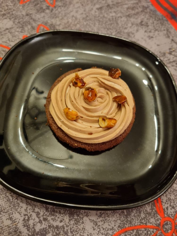 Dans une assiette à dessert : un sablé breton au chocolat, du praliné noisette caché par une ganache montée au chocolat et quelques noisettes caramélisées. 