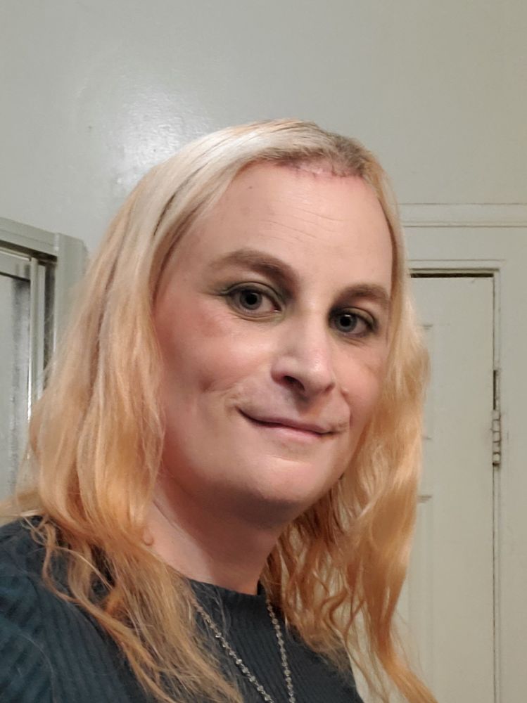 Selfie of me in a green sweater dress with wavy hair down, smiling, wearing dark eyeliner and green eye shadow