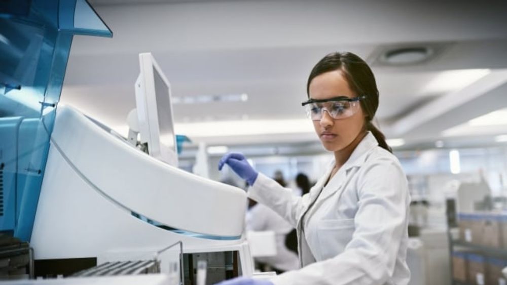 A female scientist wearing protective clothing and eyewear while working in a lab.