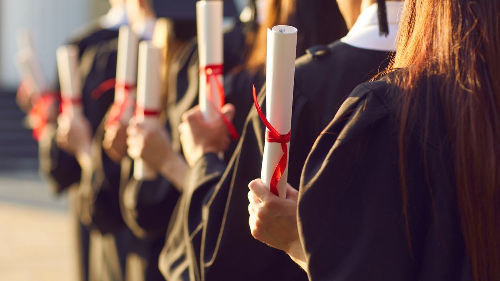 Graduates holding diplomas with red ribbons at a commencement ceremony.
