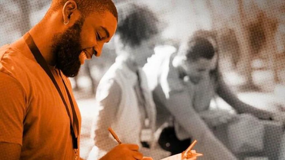 A student with a beard writes on a clipboard