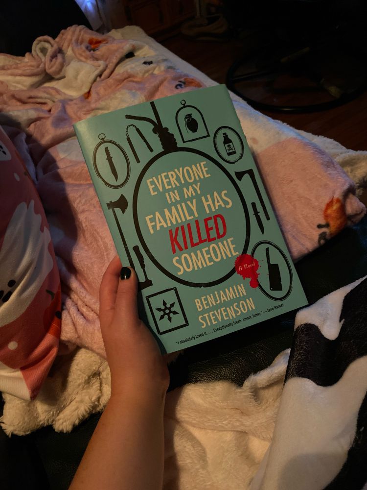 Picture of Everyone In My Family Has Killed Someone by Benjamin Stevenson being held over a pink blanket. 