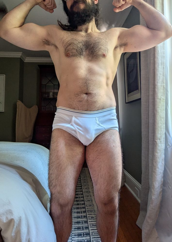 Me wearing white briefs standing facing the camera, flexing. 
