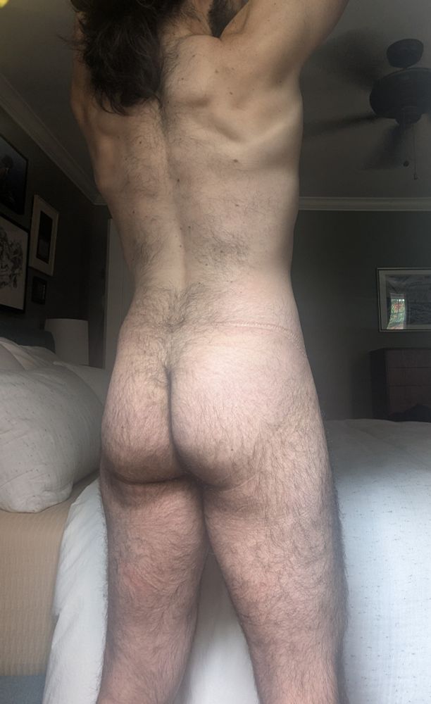 A picture of me naked from behind. I'm lifting my arms overhead. You can see my hairy back and butt.