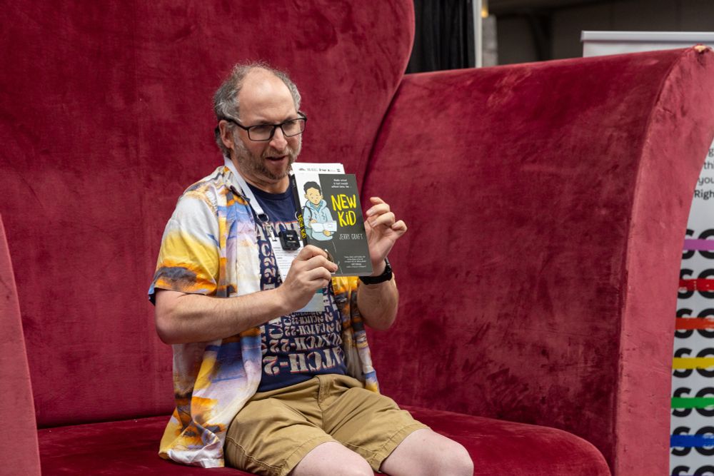 An attendee sits in the Banned Books Big Chair, holding a book titled "New Kid."