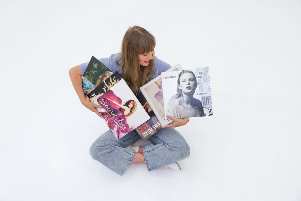 Taylor Swift sitting on ground with all of her original music in her arms