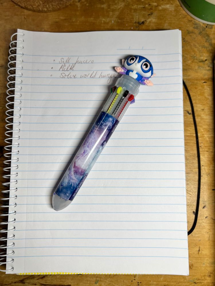 A multicolour ballpoint resting on a spiral notebook on a wooden table.