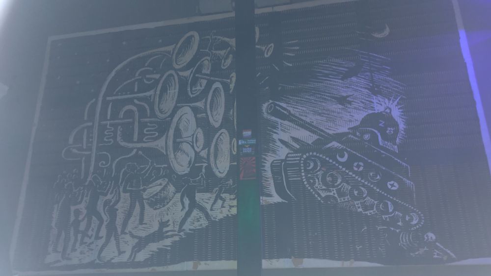 menschebmasse mit überlangen und -geoßen blechblasinstrumenten und anderen instrumenten stellen sich einem kampfpanzer entgegen (schwarz-weiße wandmalerei)