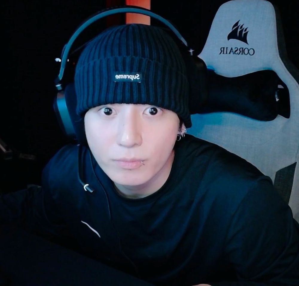 Jungkook on live with a beanie and headphones on, looking positively round as he looks at the camera 
