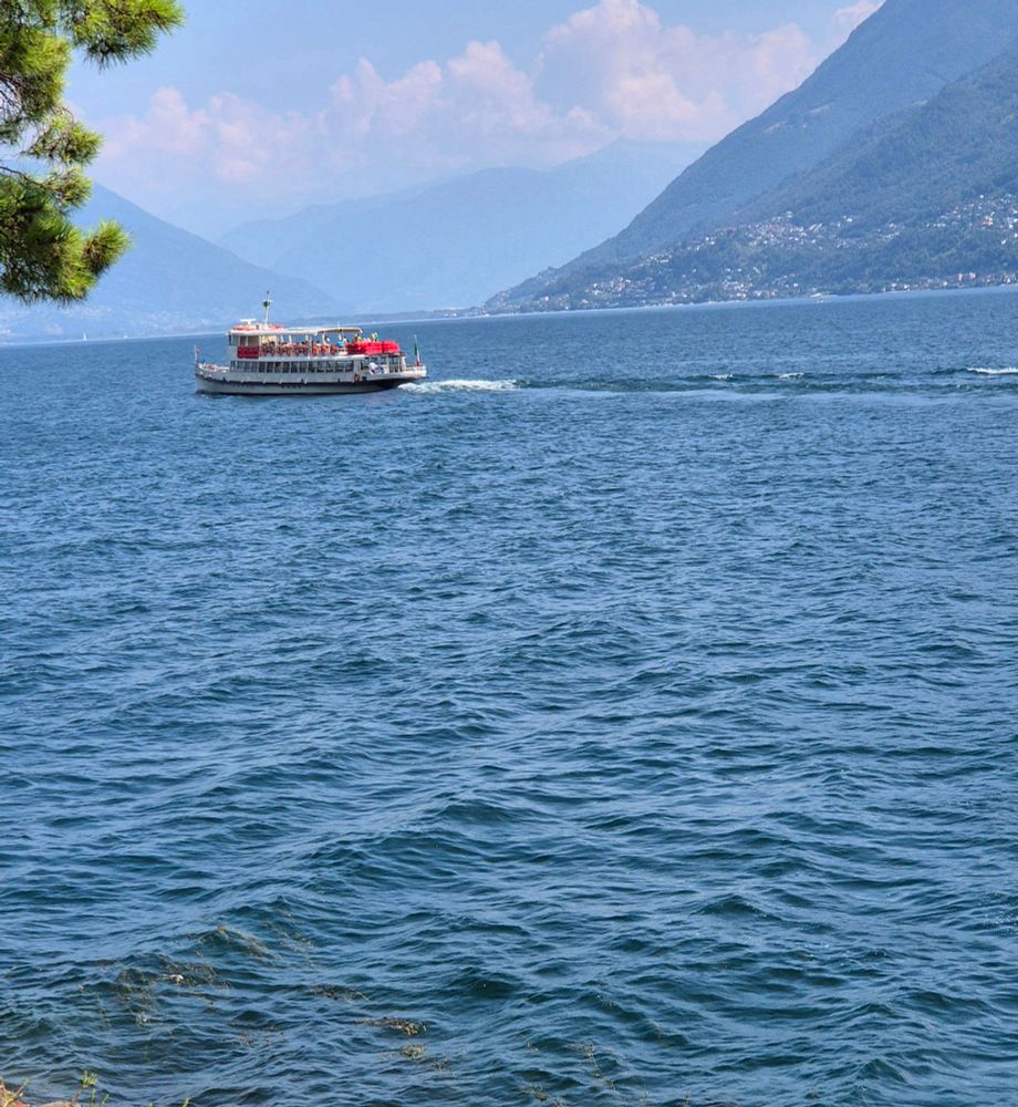 Blauer See und ein Kursschiff. Berge. Blauer Himmel mit weissen Wolken.