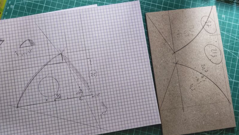 Croquis sur papier petits carreaux représentant un triangle avec un bord arrondi. À côté, le tracé sur du carton gris. Le tout sur un tapis de découpe auto cicatrisant vert.