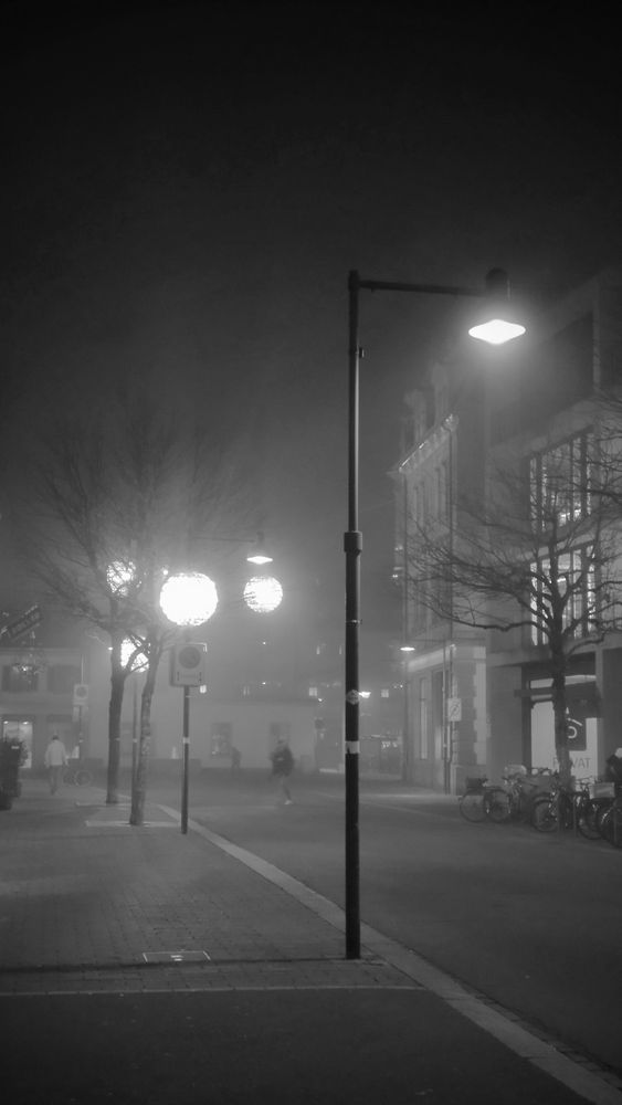 Lamp post and Chrismas light balls on a foggy street, small trees and houses in the background