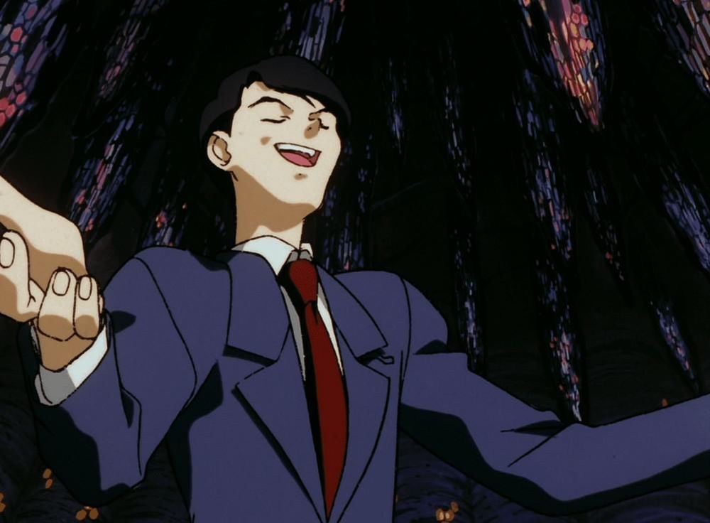 Image tirée d'un anime. Un personnage d'allure masuline, en costar-cravate, est montré en contre plongée, les bras écarté, les yeux fermés et la tête un peu en arrière ; comme s'il faisait un monologue, très sûr de lui. L'arrière-plan de l'image est essentiellement sombre avec des taches de lumières colorées