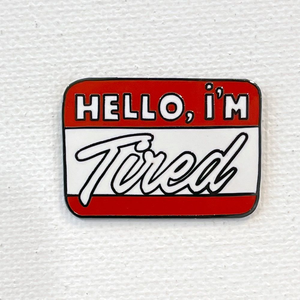 A rectangular pin that looks like a red and white name tag. It says "Hello, I'm tired".