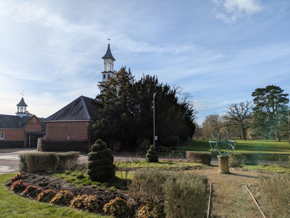 A garden and a sculpture in front of buildings and a blue sky.